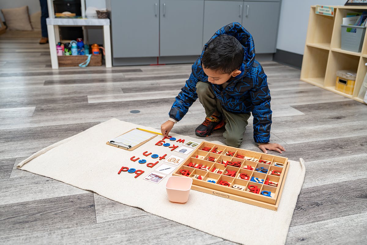 Child kneeling on floor, arranging letter tiles on a mat