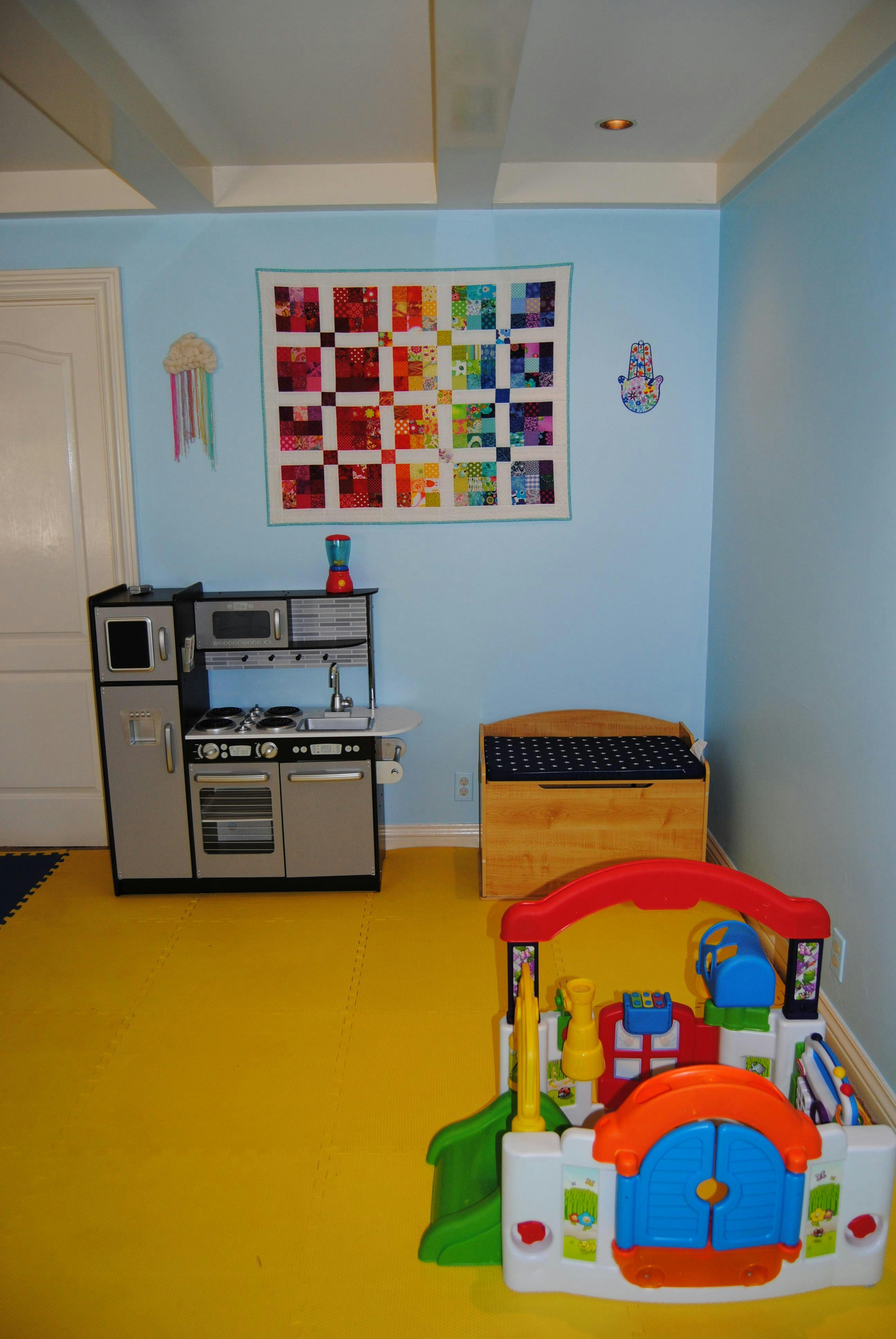 Playroom with toy kitchen, toy house, and colorful quilt on the wall