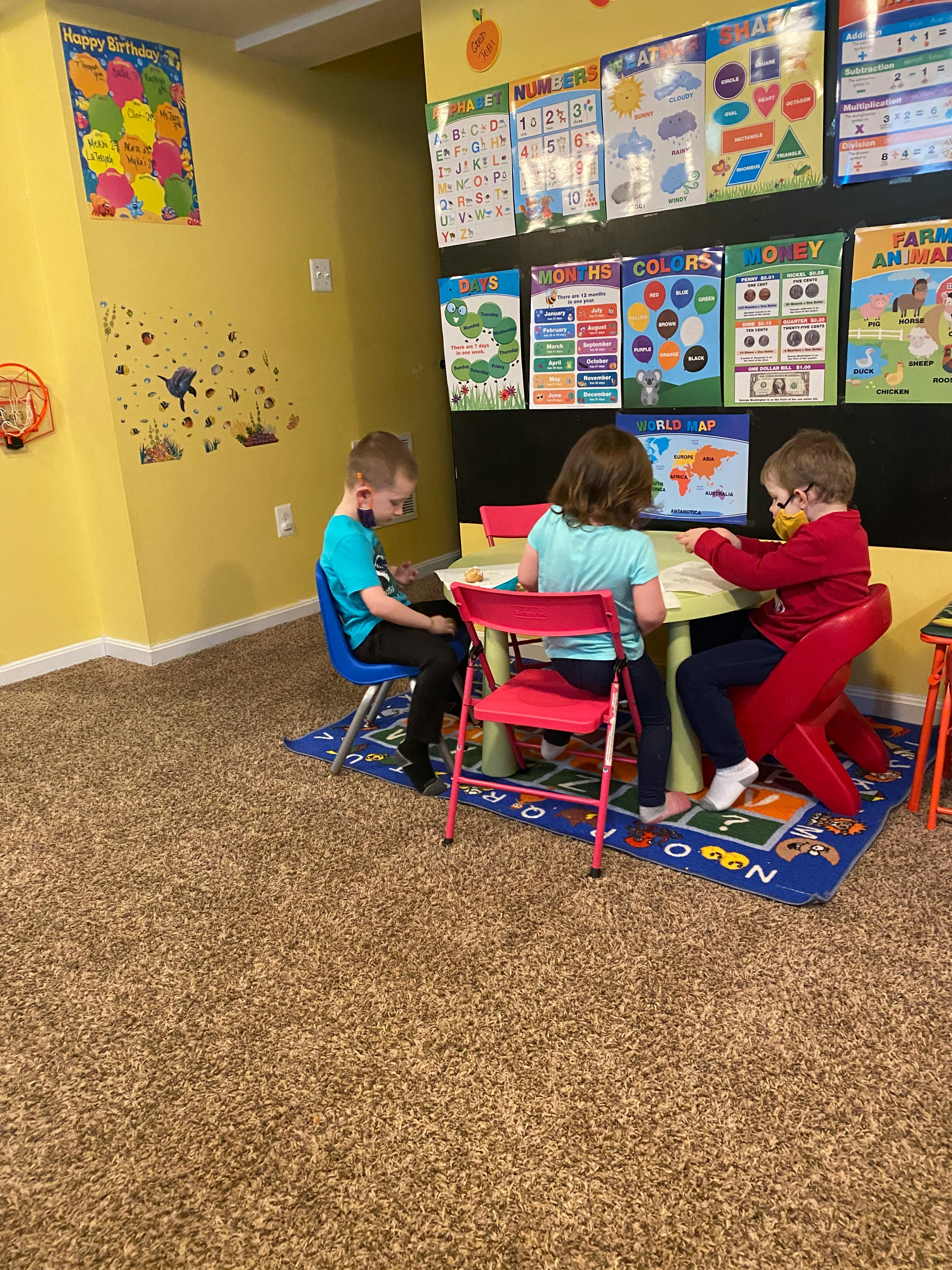 Three children sitting at a small table in a classroom