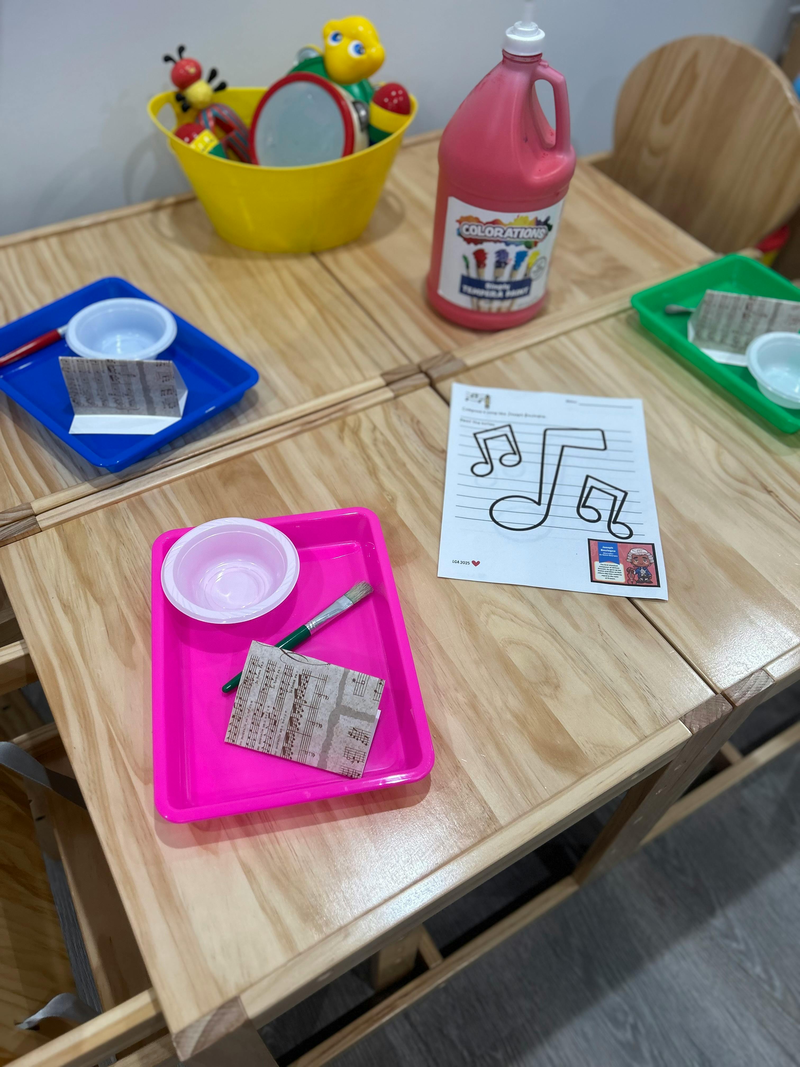 Craft supplies on a wooden table, including paint, trays, and a music note drawing