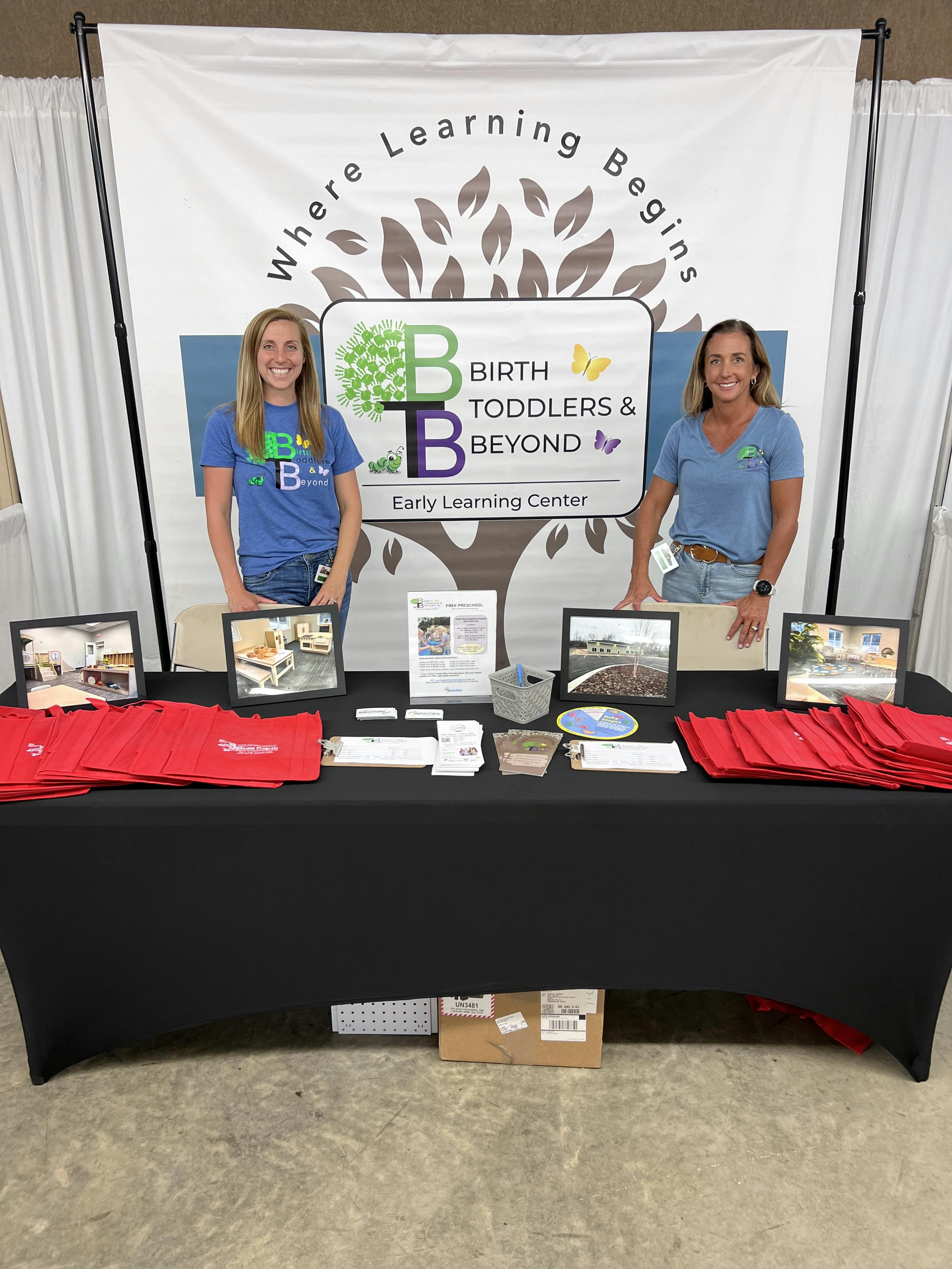 Two women standing behind a table with the text "Birth Toddlers & Beyond"