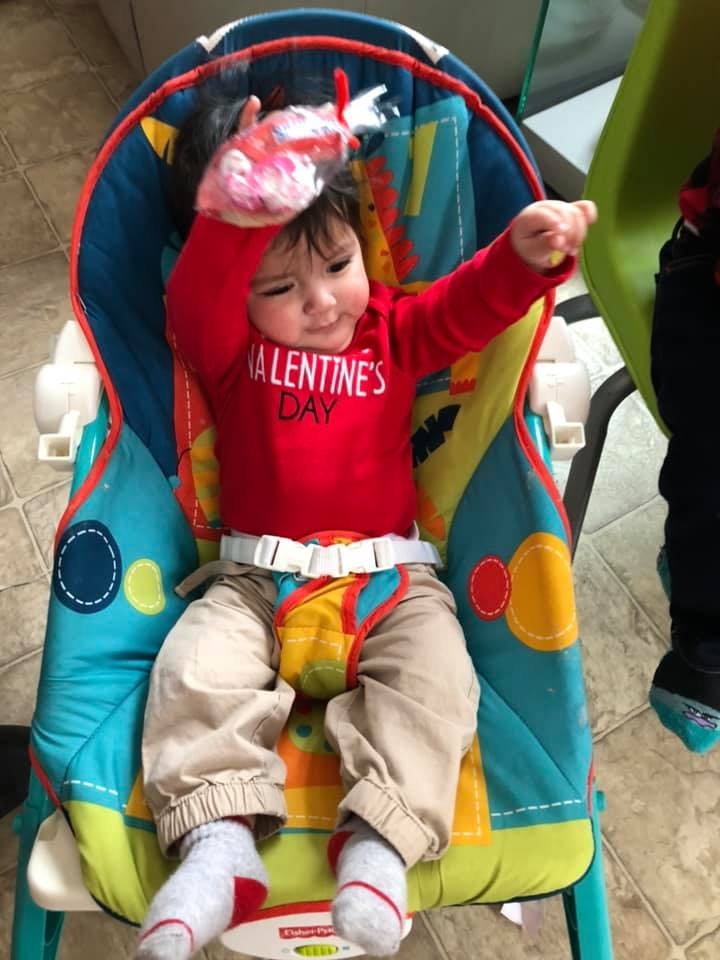 Child in a red shirt that says "Valentine's Day" sitting in a baby bouncer