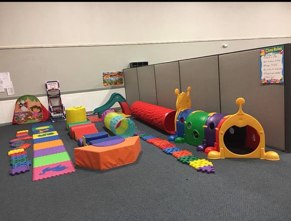 Indoor soft play area with colorful mats, blocks, tunnels, and a caterpillar climber