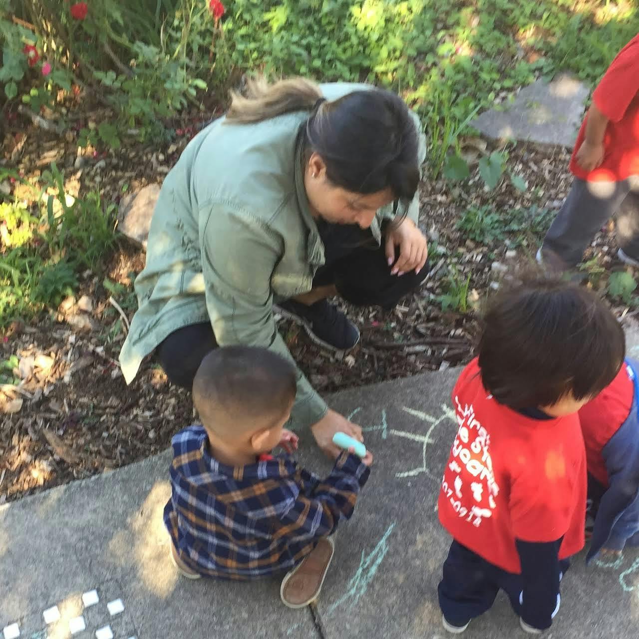 Person and two children drawing with chalk on pavement