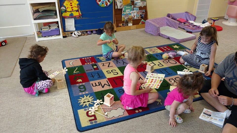 Children playing on an alphabet rug in a classroom
