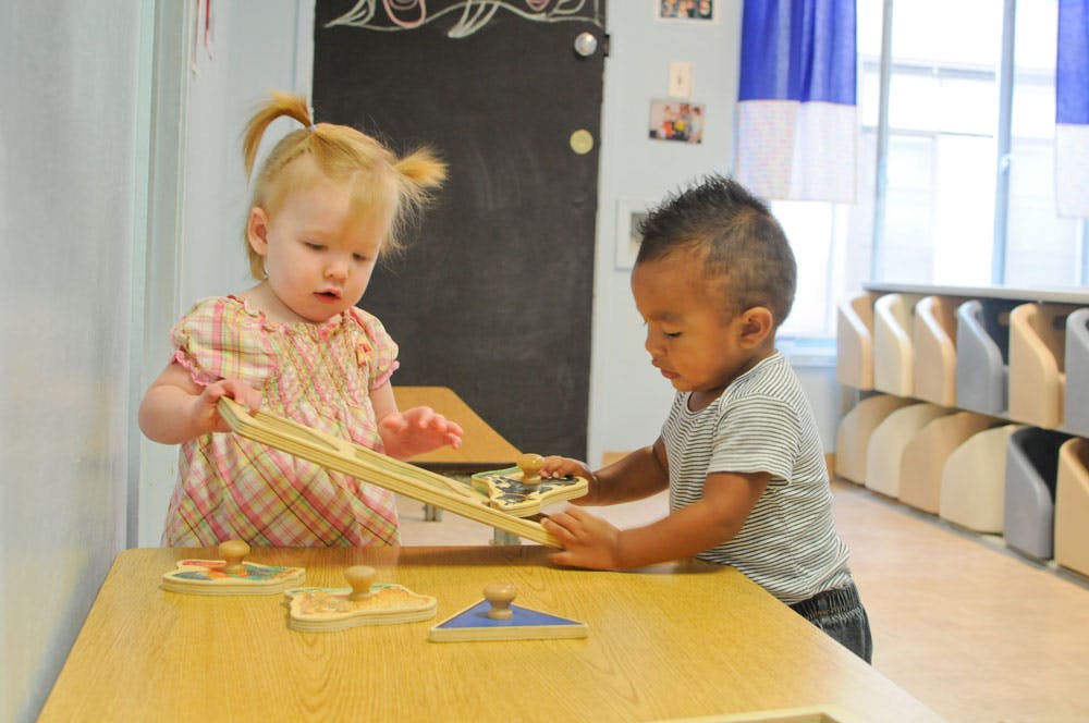 Two children playing with wooden puzzles at a table in a classroom