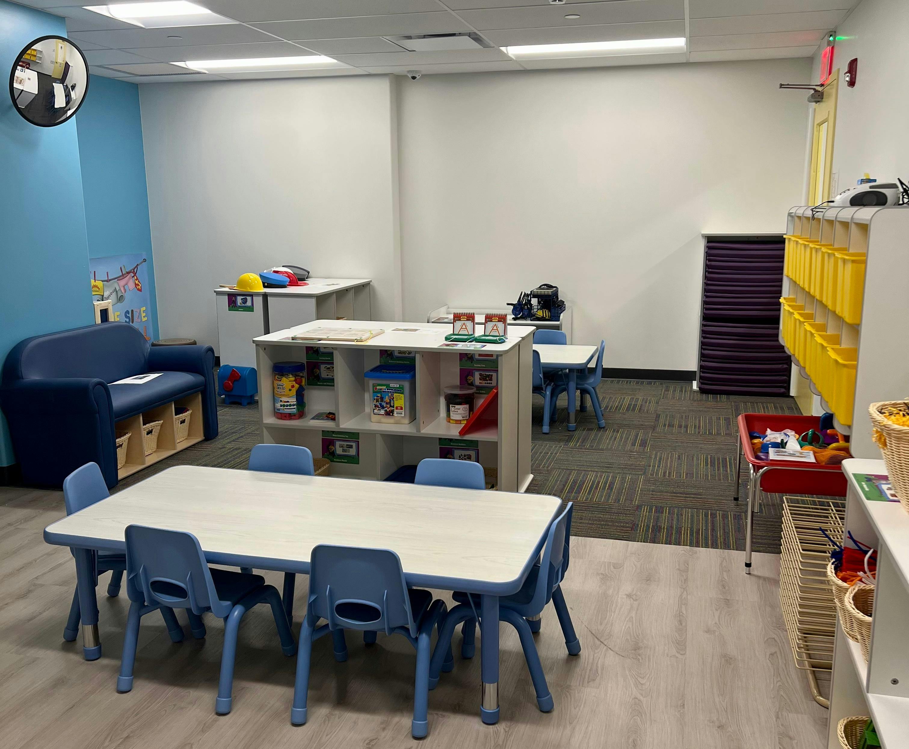 Classroom with small tables and chairs, a blue couch, and storage shelves