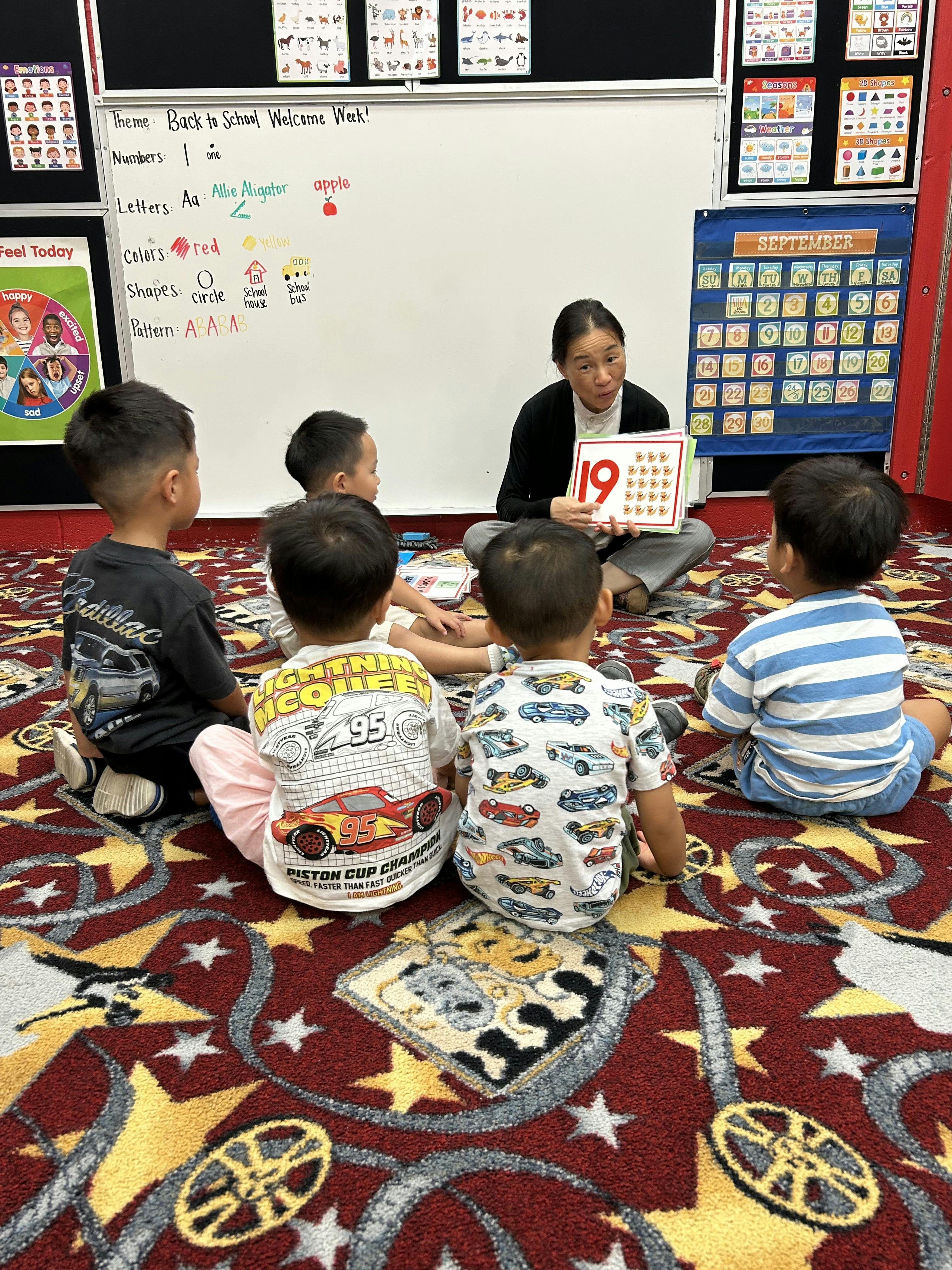 Teacher holding a number 19 flashcard for a group of children in a classroom