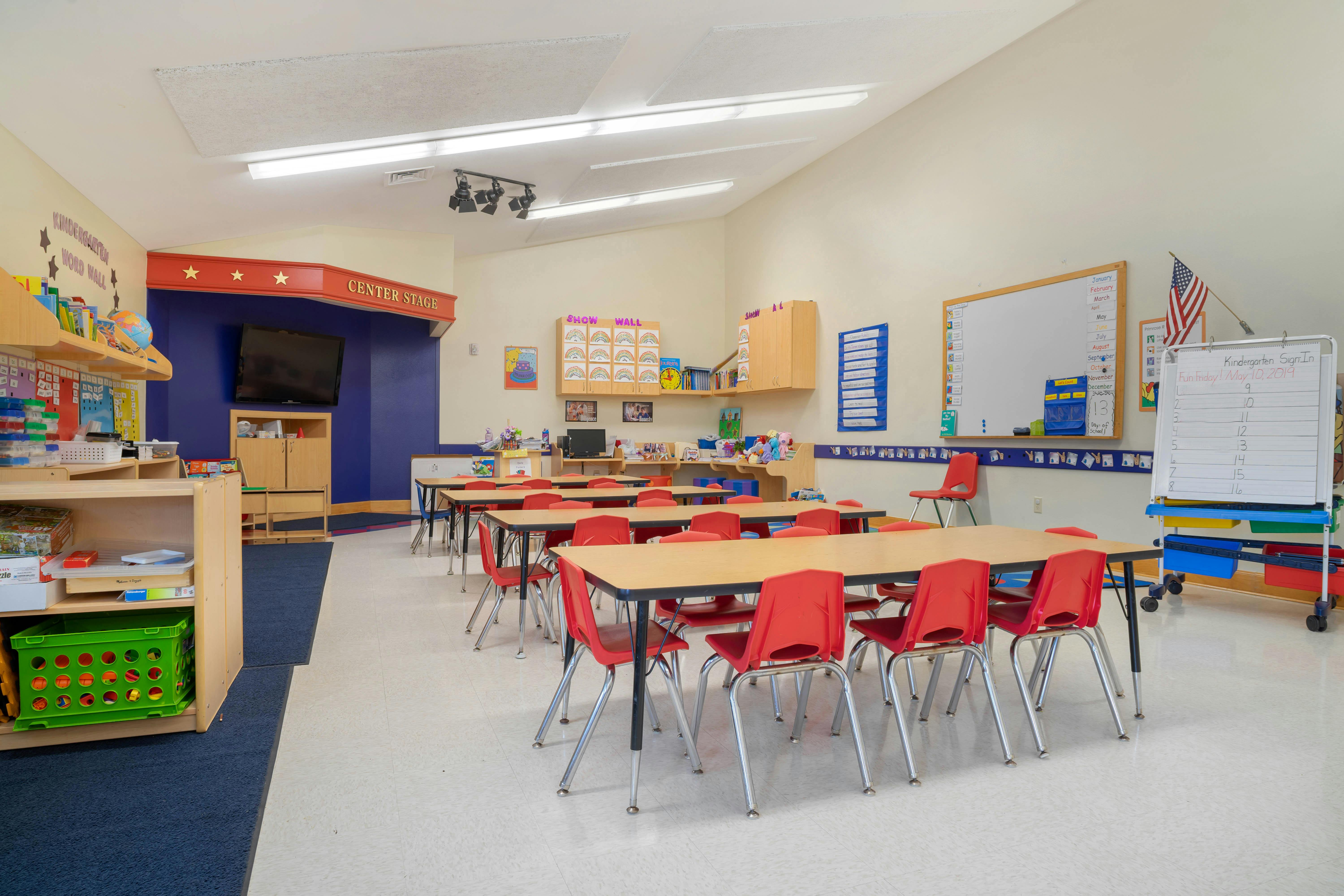 Empty kindergarten classroom with small tables and red chairs