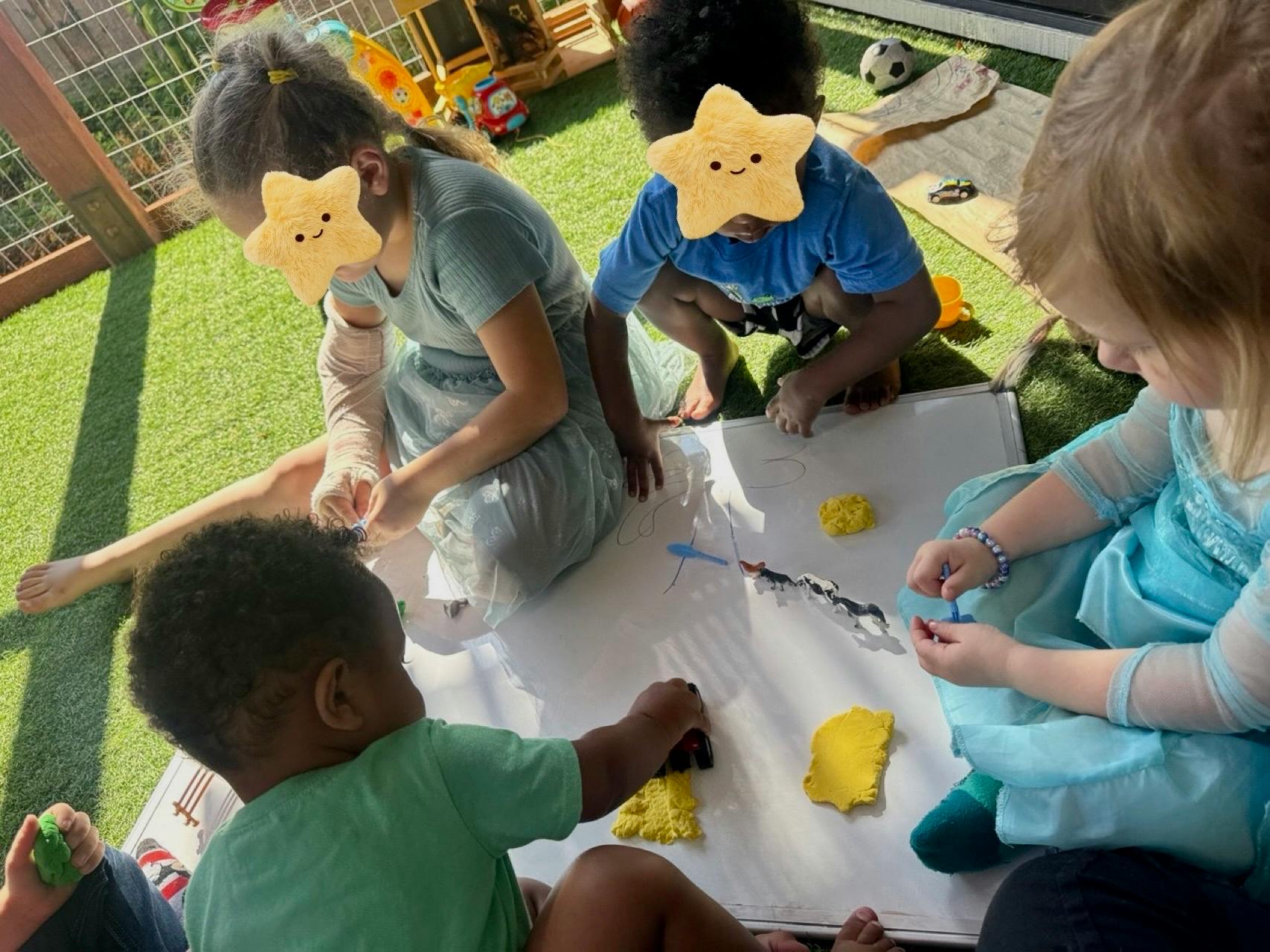 Four children playing with clay and small toys on a white board outdoors