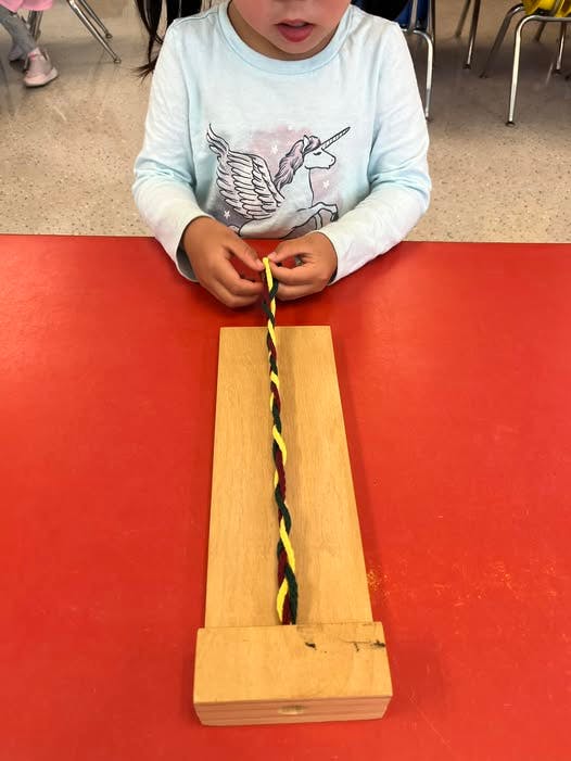 Child braiding yellow and black string on a wooden board