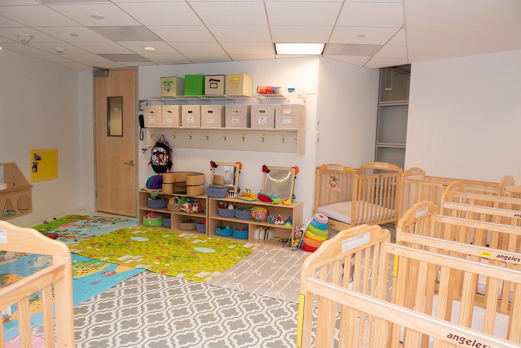 A room with wooden cribs, play mats, shelves with toys, and storage