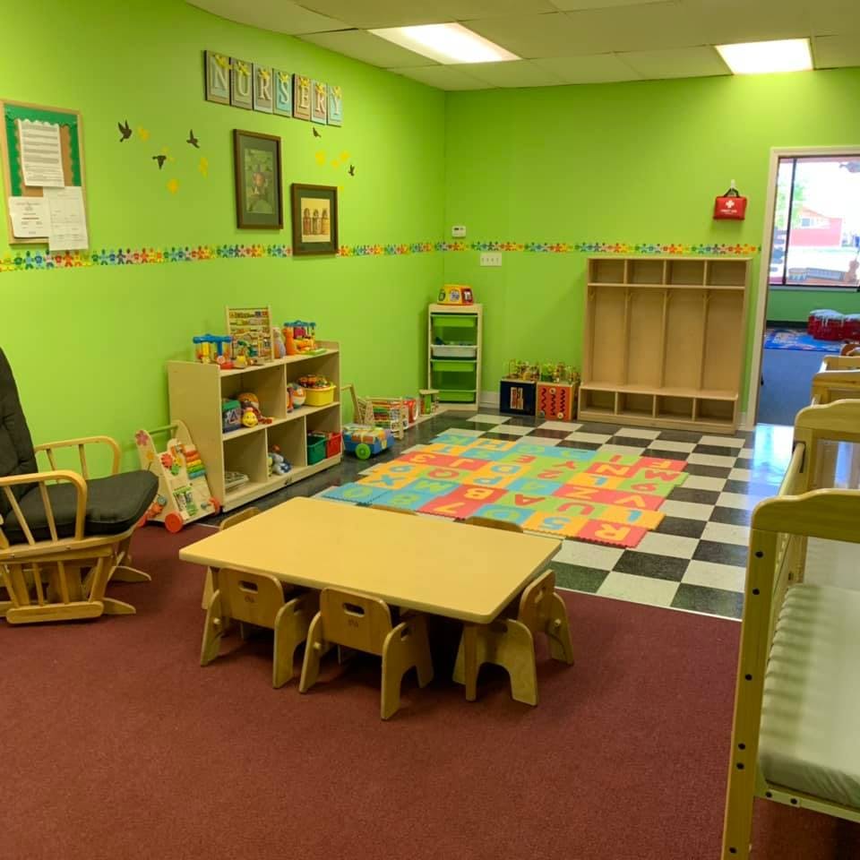 Classroom with small table and chairs, shelves with toys, and a play mat