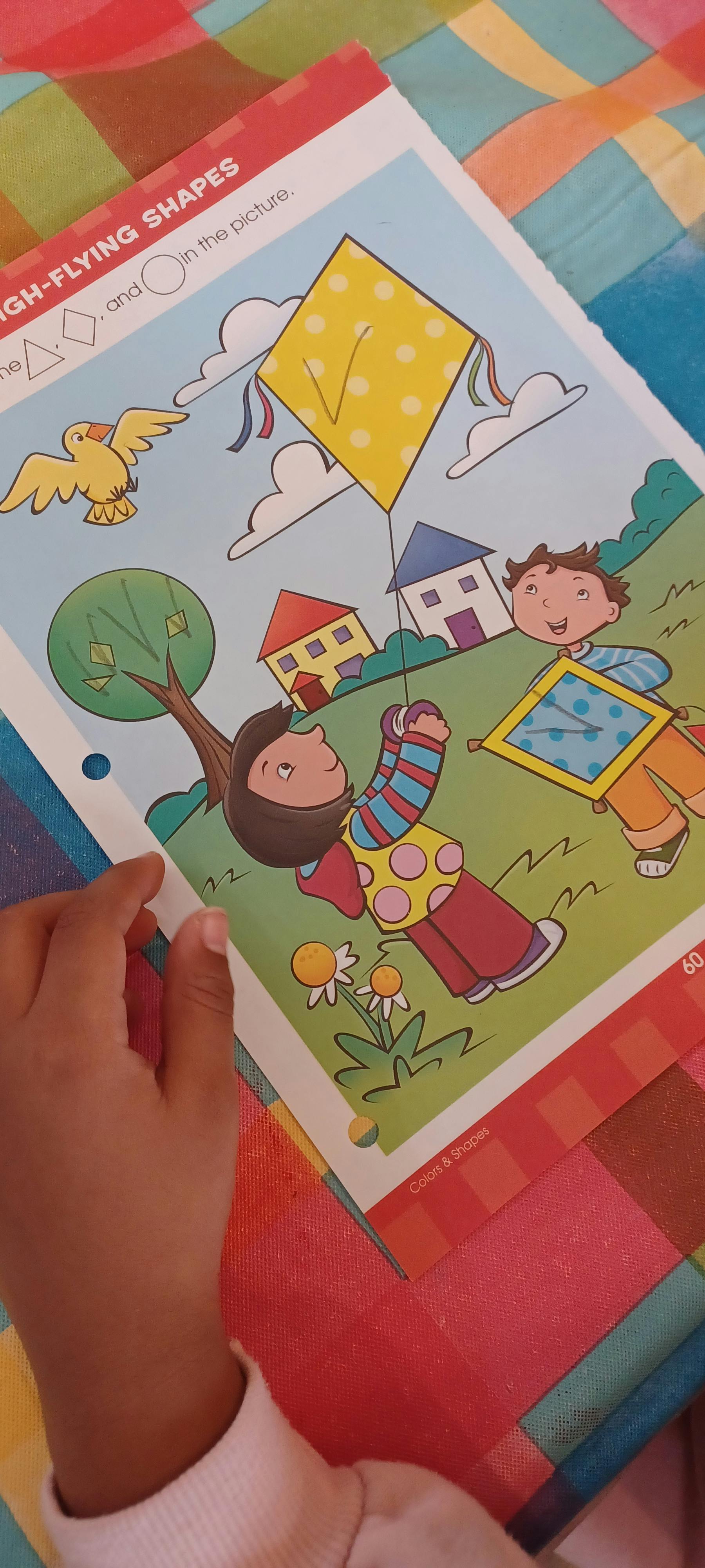 Child's hand on a workbook page with cartoon children flying kites