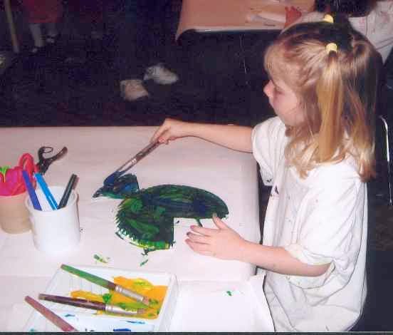 Child painting a green shape on paper with a paintbrush