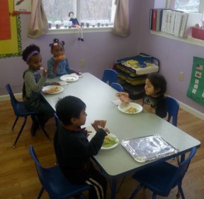 Four children eating at a table in a classroom