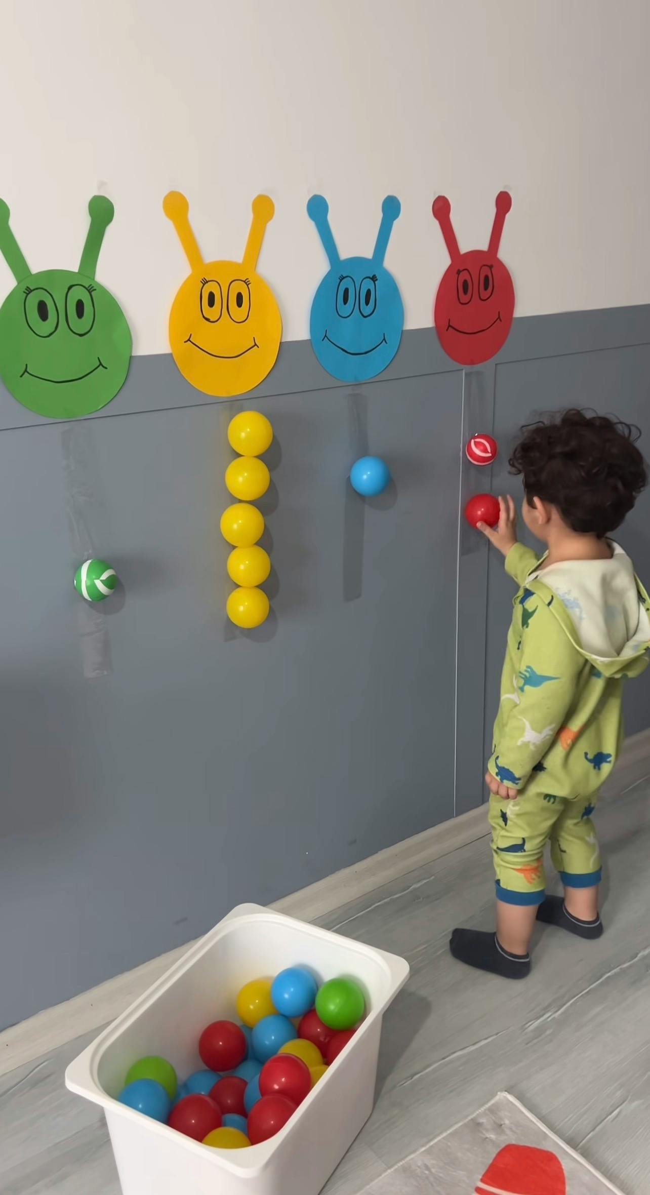 Child playing with colorful balls on a gray wall with cartoon faces