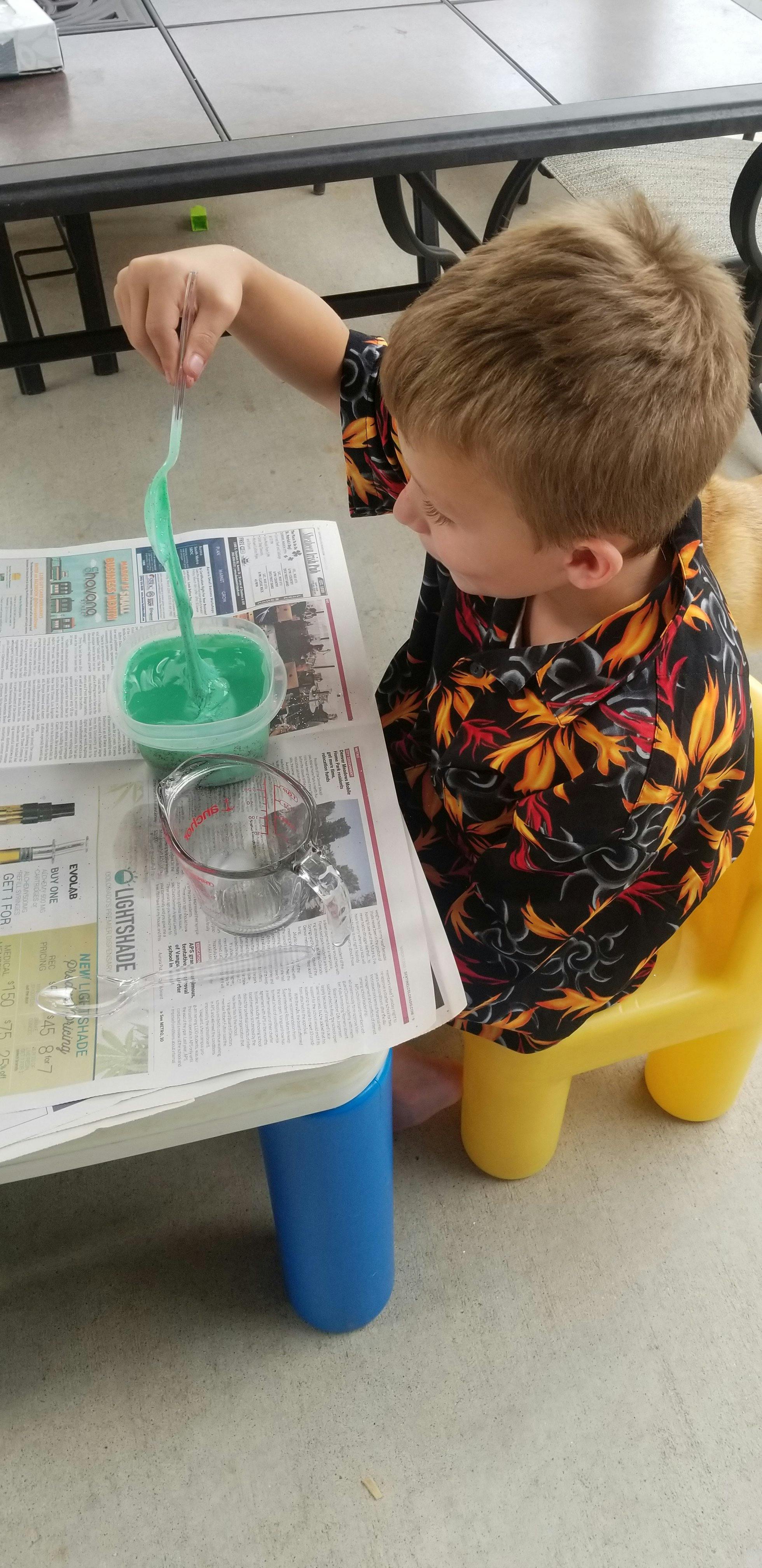 Child playing with green slime on a newspaper-covered table