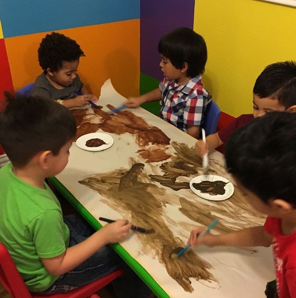 Children painting with brown paint at a table