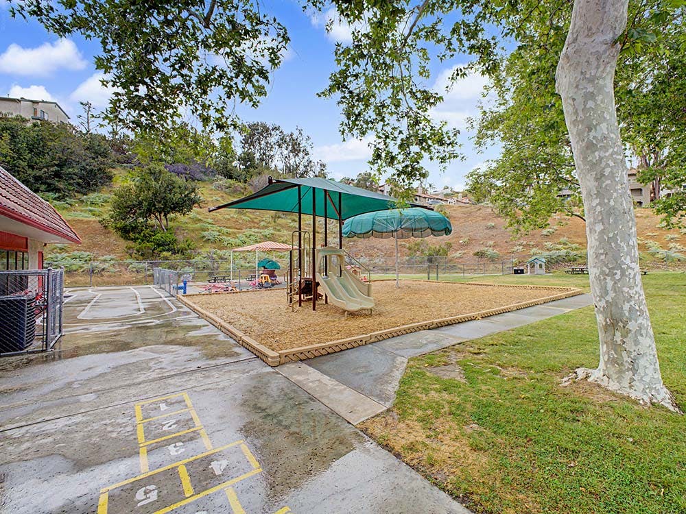 Empty outdoor playground with slides, shade covers, and a hopscotch court