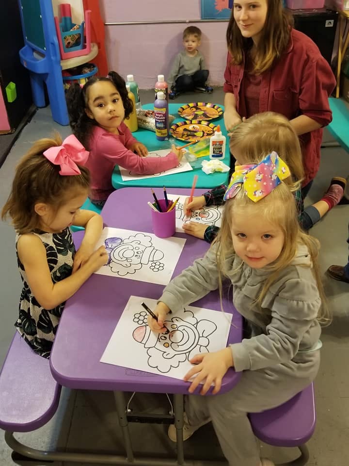 Children coloring at tables with an adult nearby