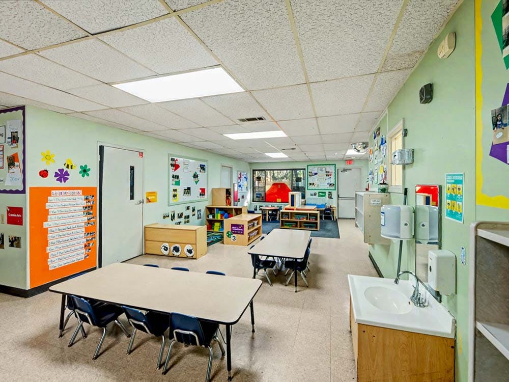 Empty classroom with small tables and chairs, and a sink area