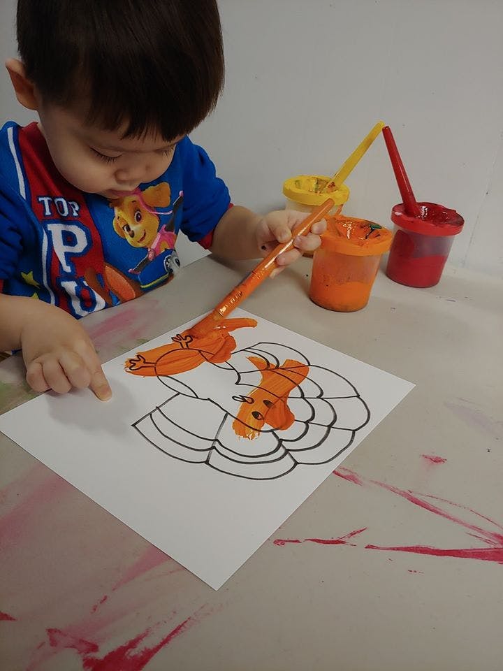 Child painting a pumpkin outline on paper