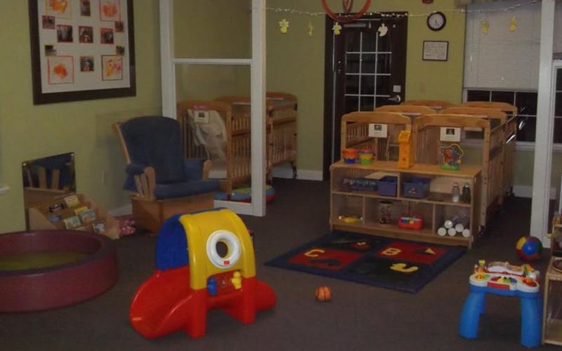 A playroom with cribs, a small slide, a ball pit, and a rocking chair