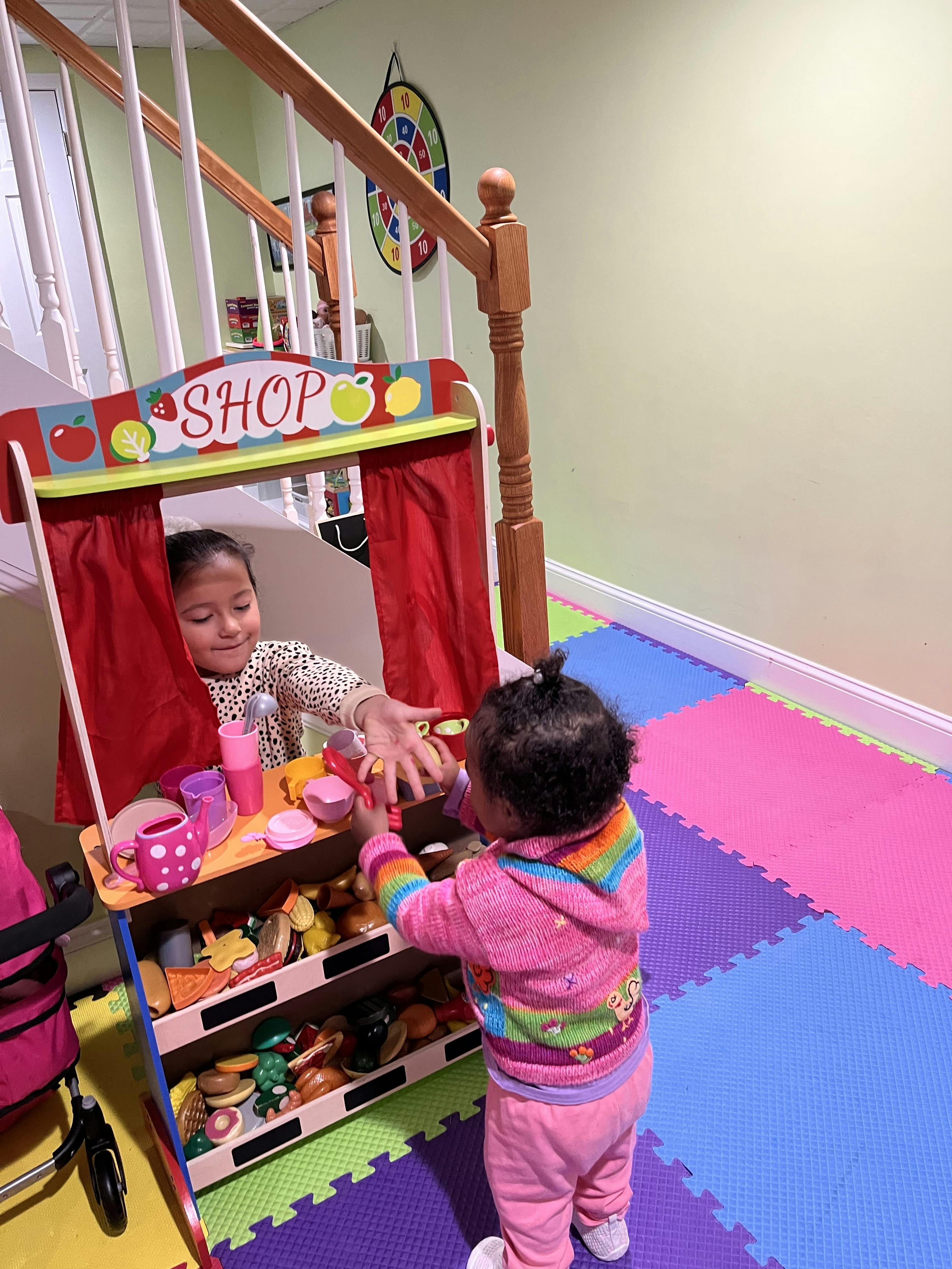 Two children playing with a toy shop stand, one behind the counter and one in front
