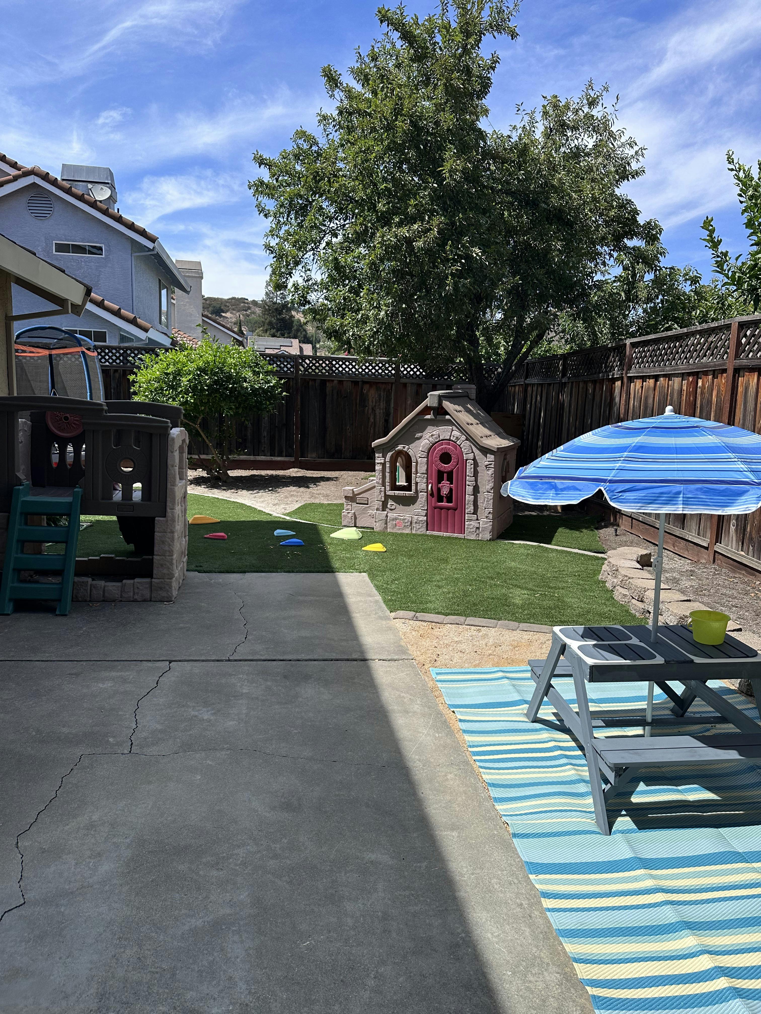 Playhouse and children's picnic table with umbrella in a backyard