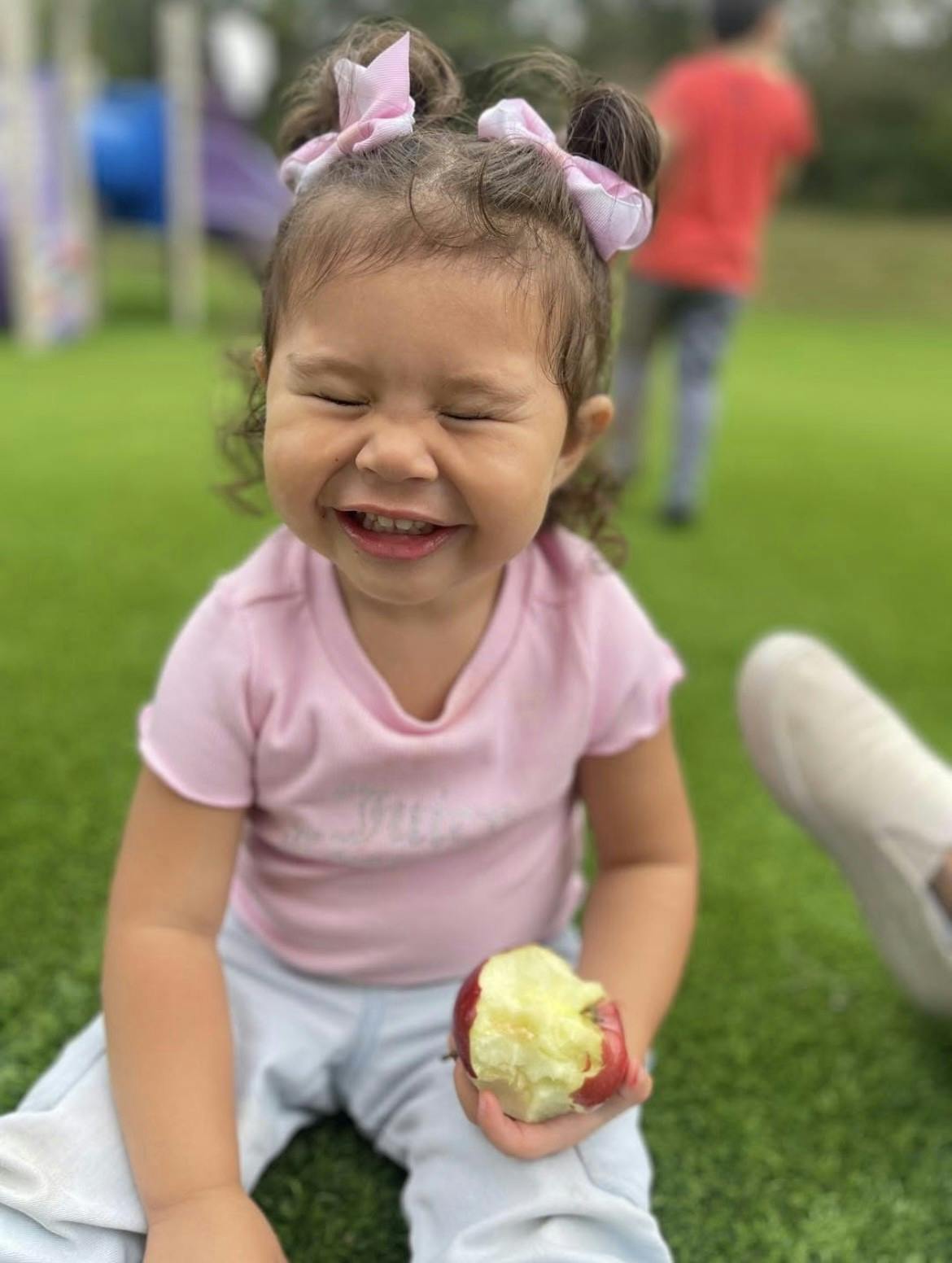 Child with pigtails holding a partially eaten apple