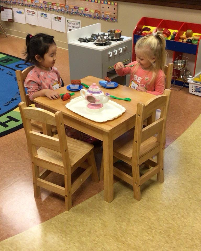 Two children playing with a toy tea set at a small table