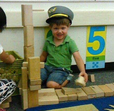 Child in a pilot hat playing with wooden blocks