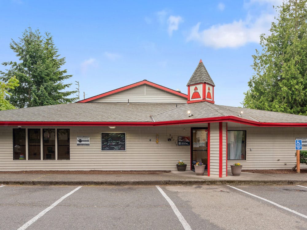 Exterior of a building with a red roof, a small tower, and a parking lot in front