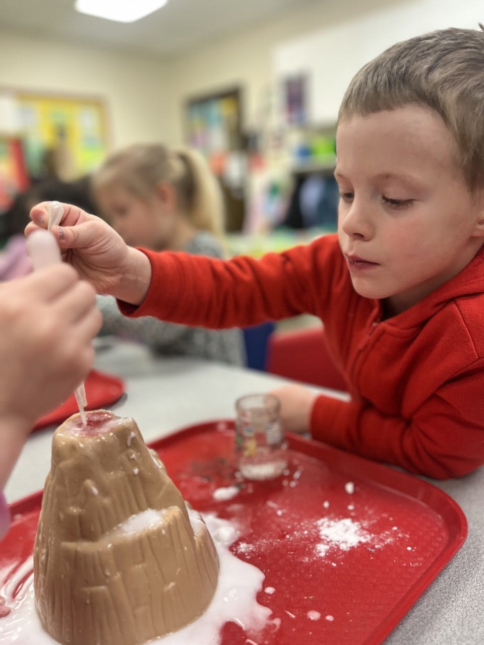 Child pouring liquid into a model volcano that is erupting foam