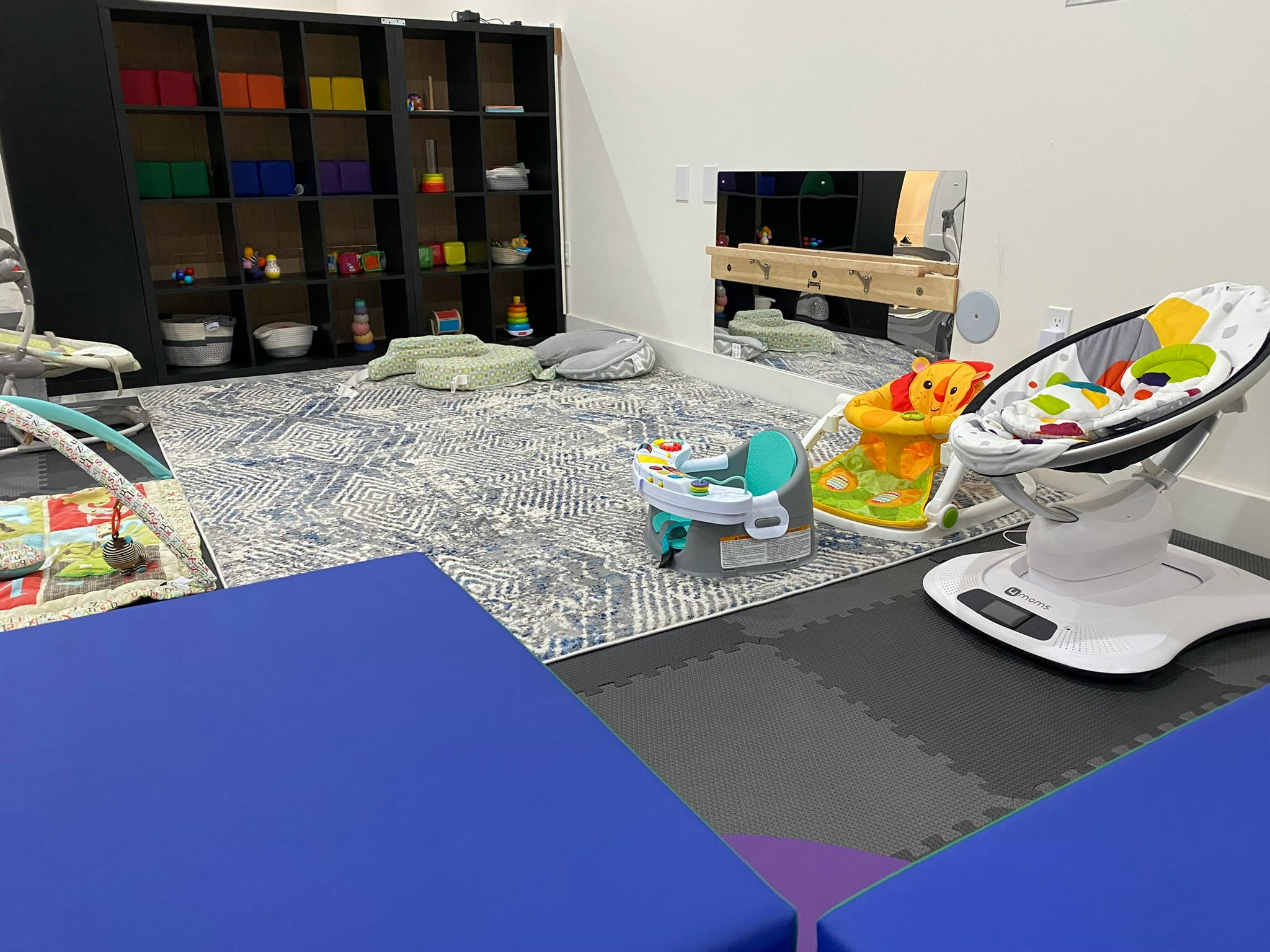 Playroom with baby seats, play mats, and shelves with shelves of toys
