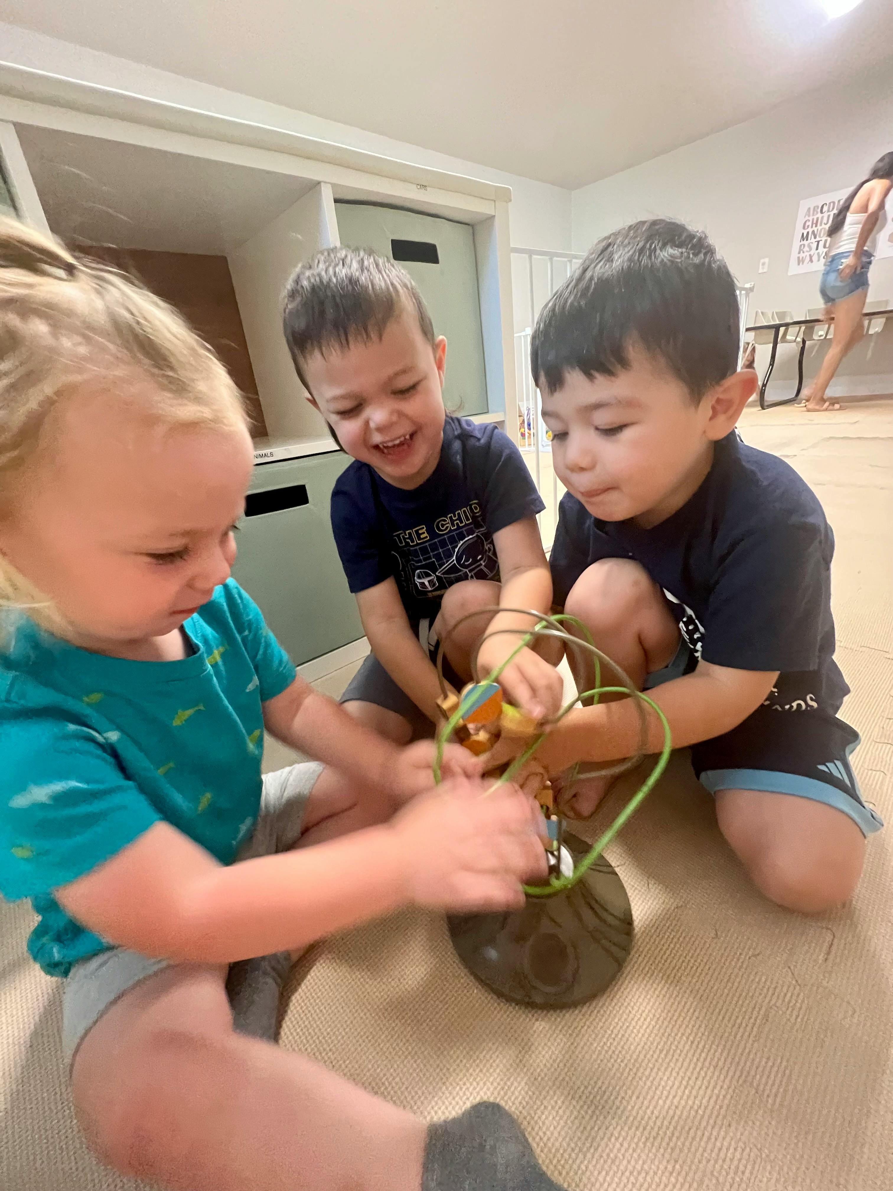 Three children playing with a bead maze toy on the floor