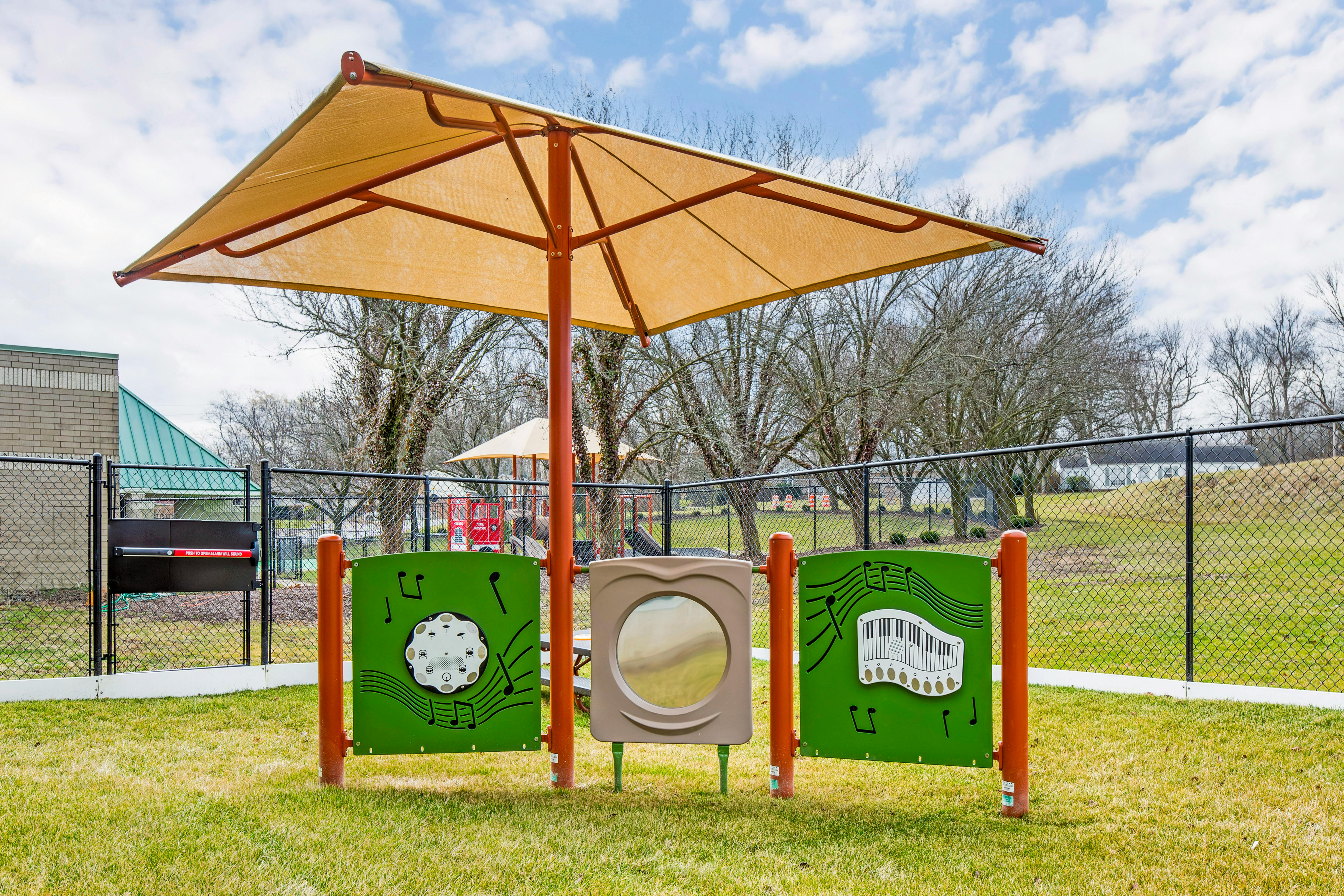 Shaded musical play panels on a grassy area with a fence in the background