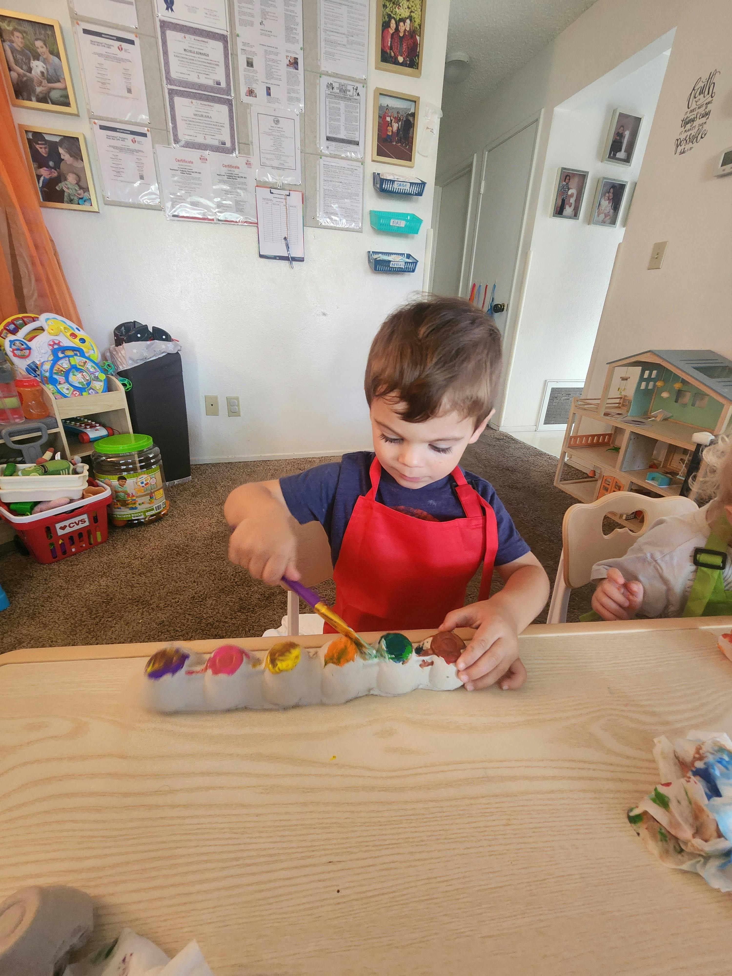 Child in a red apron painting at a table