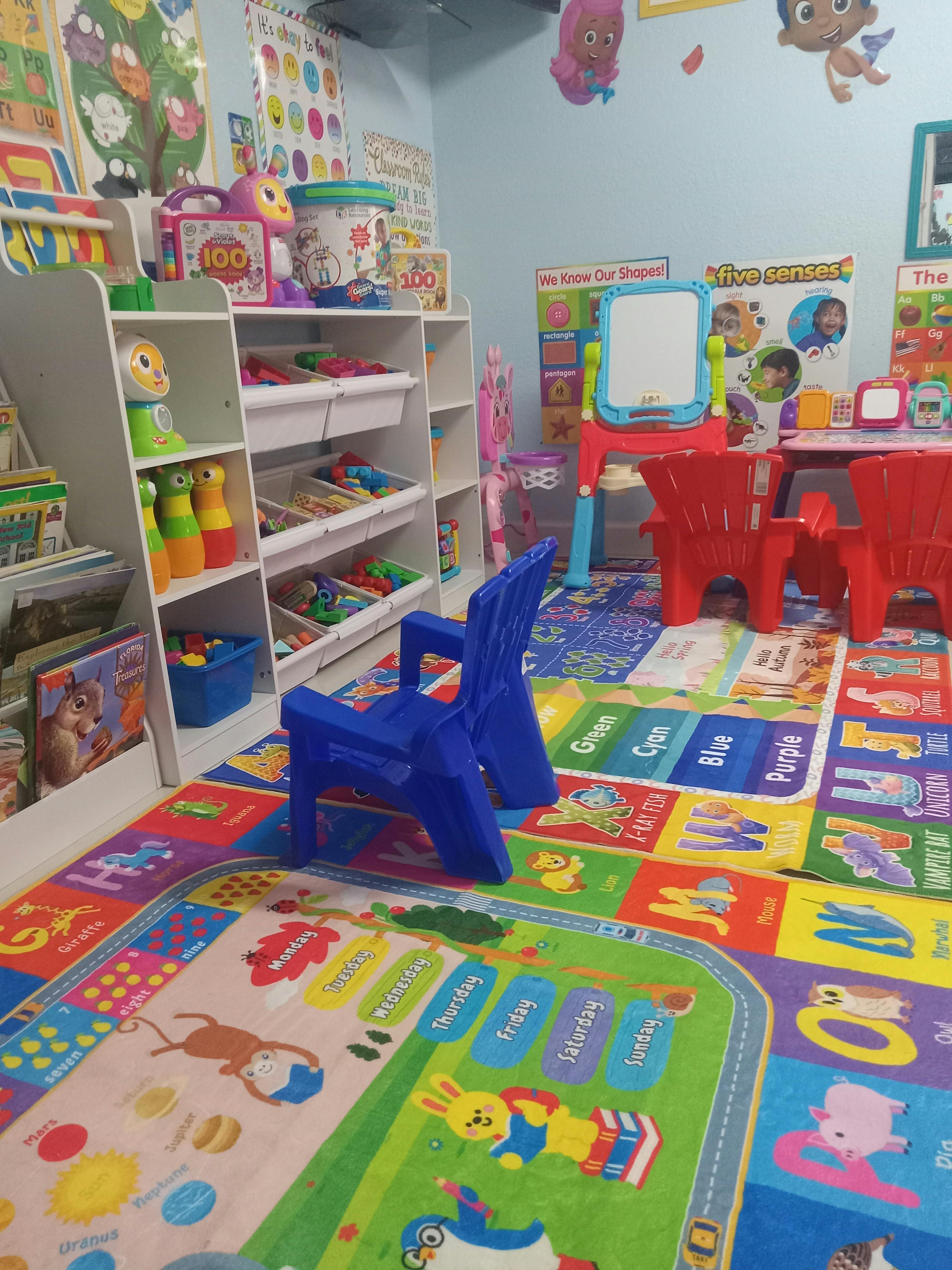 Colorful playroom with a children's rug, small plastic chairs, and toy shelves