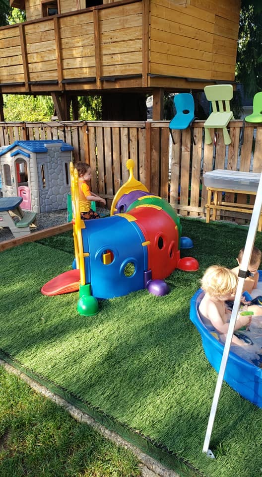 Child playing near a colorful caterpillar tunnel and a wading pool