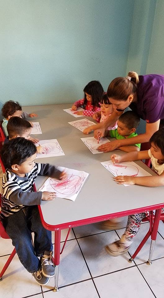 Adult helping children color at a table in a classroom