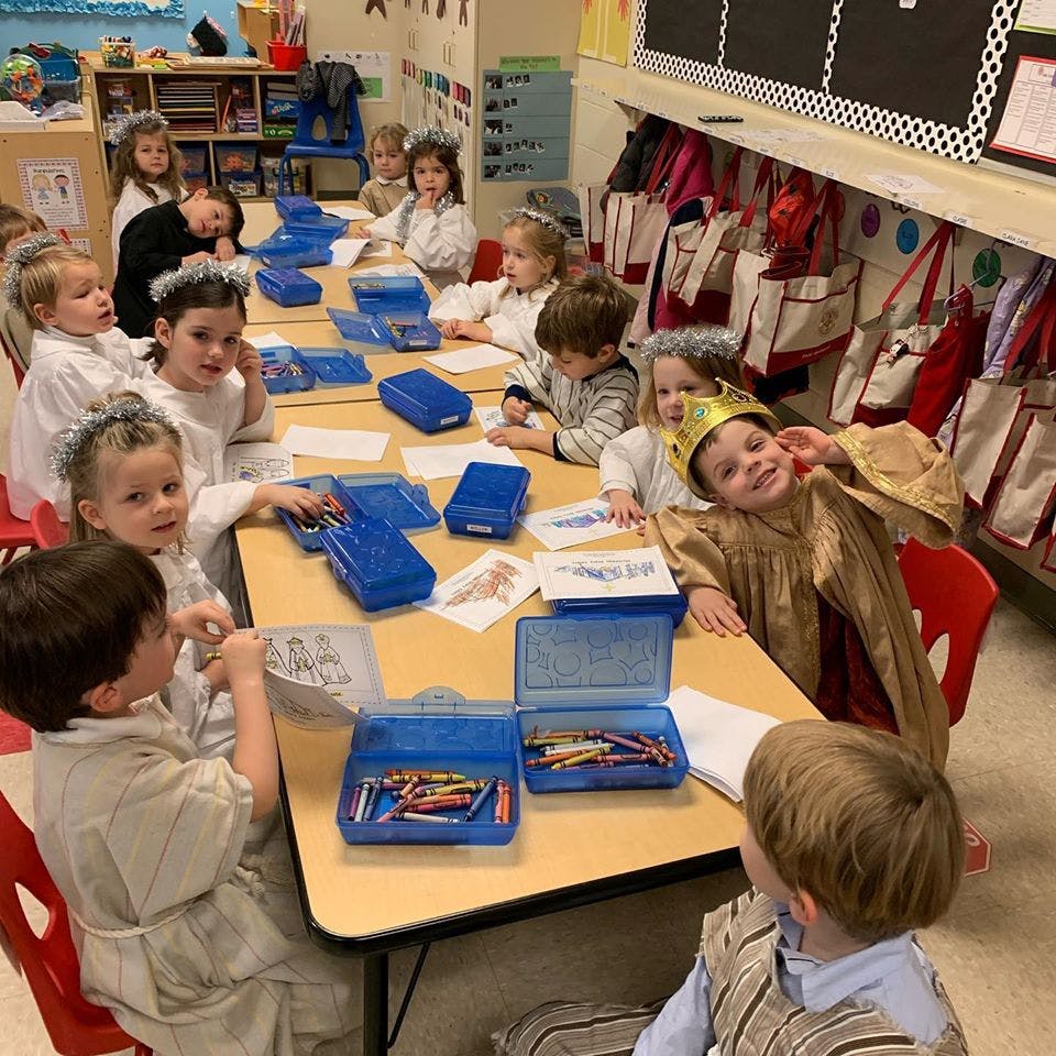 Children in costumes sitting at a table with art supplies in a classroom