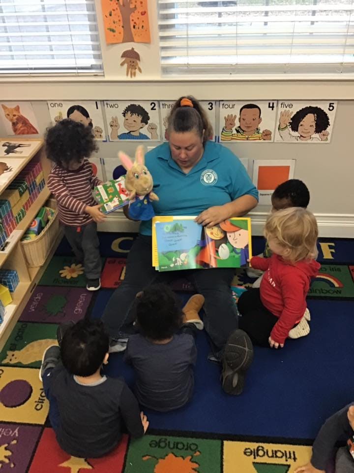 Adult reading a book to several children in a classroom