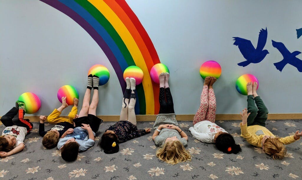 Children lying on their backs with rainbow balls on their feet