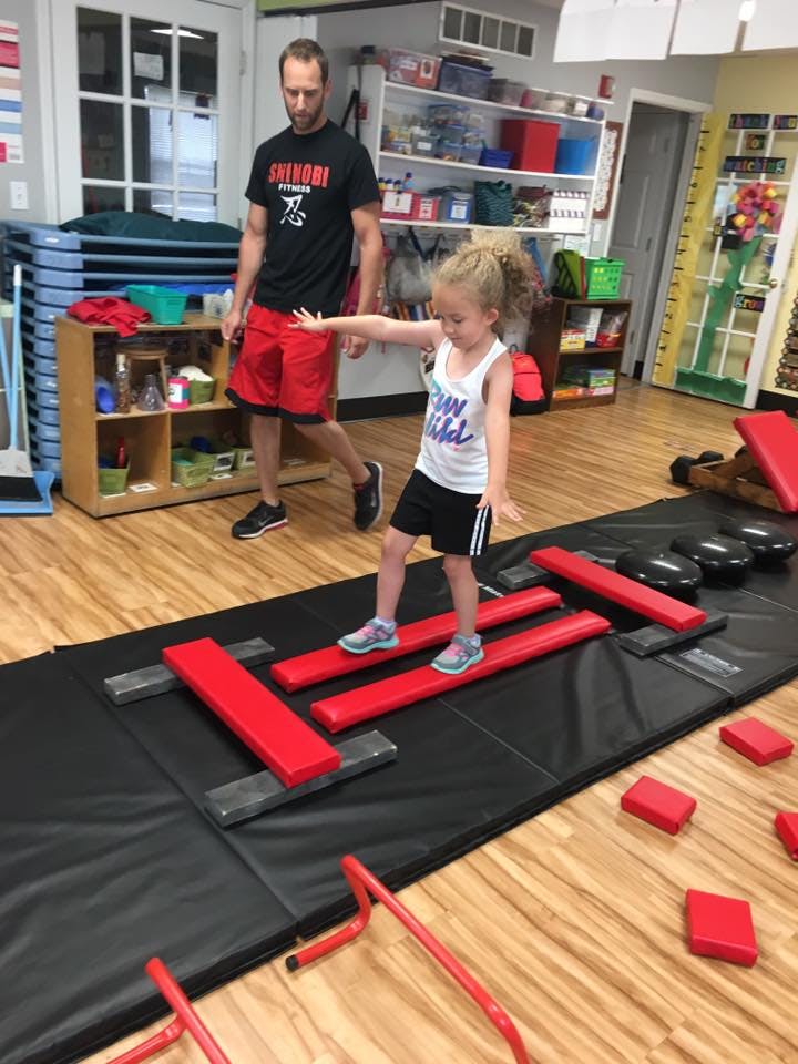 Child balancing on red beams on a black mat with a person standing nearby