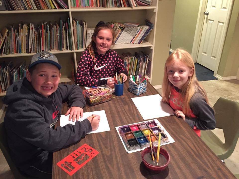Three children sitting at a table with art supplies