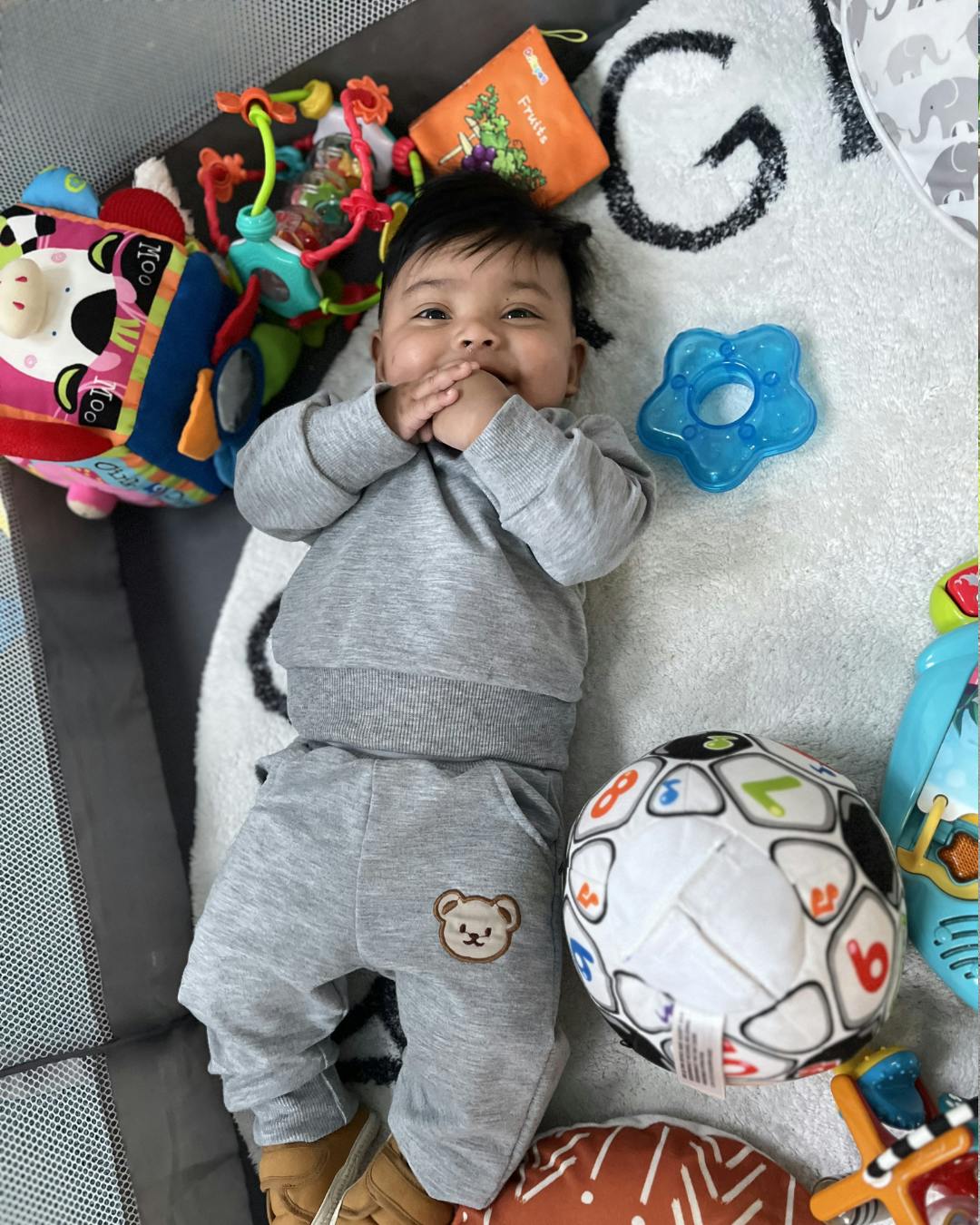 Baby lying down with hands near face, surrounded by toys