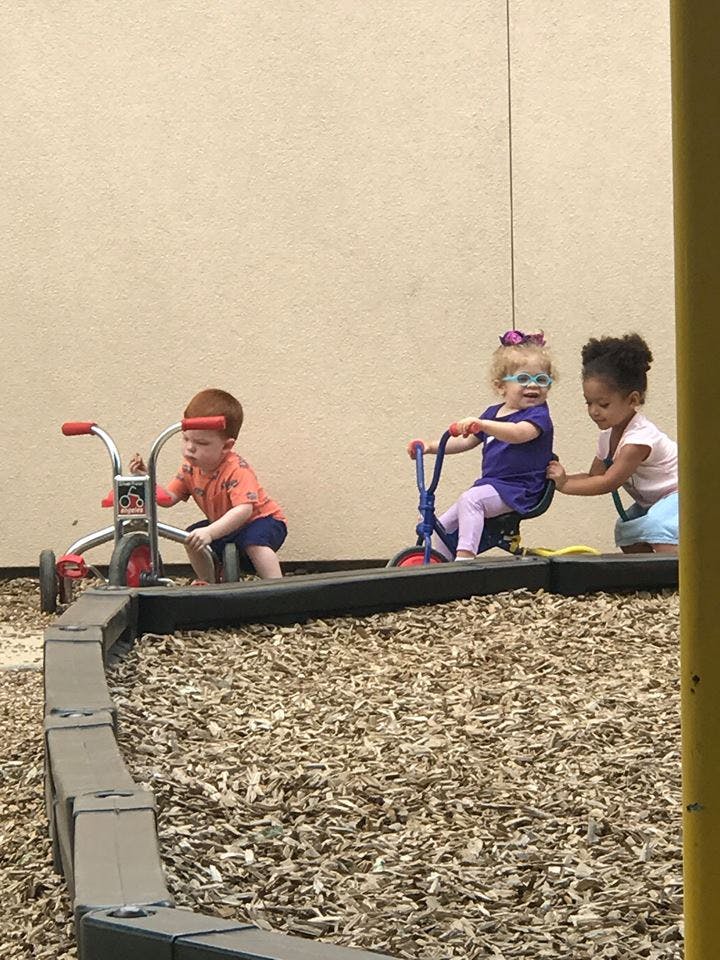 Three children playing with tricycles on wood chips