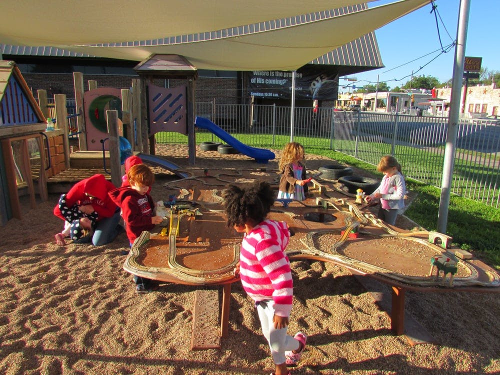Children playing in a sandbox with a play structure in the background